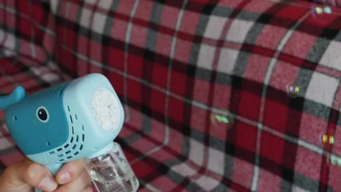 Person Shooting Soap Bubbles from Blue Whale Toy Against Red Plaid Background Stock Footage 339176827