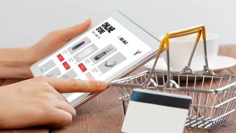 Person shops online using a tablet while sitting at a wooden table with a cup Stock Photos