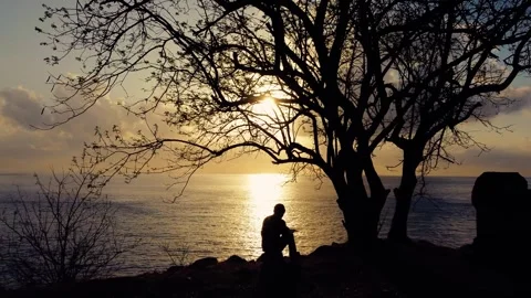 A person sits beneath a tree by a grave at island Bali Stock Footage 288738060