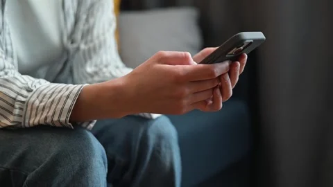 A person sits on a couch, focused on their smartphone while engaging with it. Stock Footage 338446074