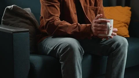 A person sits on a couch holding a mug in a cozy indoor space. The individual Stock Footage 339097583