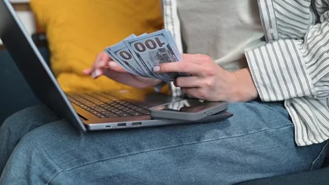 A person sits on a couch with a laptop, counting cash and preparing to handle Stock-Footage 338446338