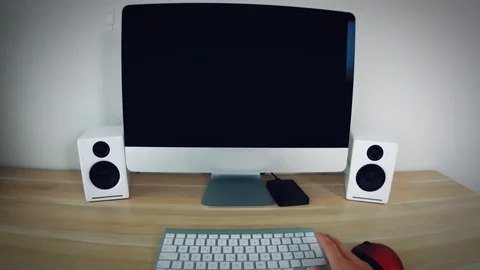 Person sits down at his desk in the home office and starts his PC, logs in Stock Footage 128653055