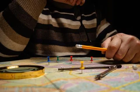 A person sits at a table with a map spread out. They use a pencil to mark spo Stock Photos