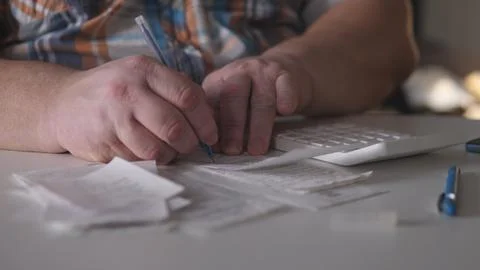 Person sits at a table writing notes on receipts while using a calculator in an Stock Photos