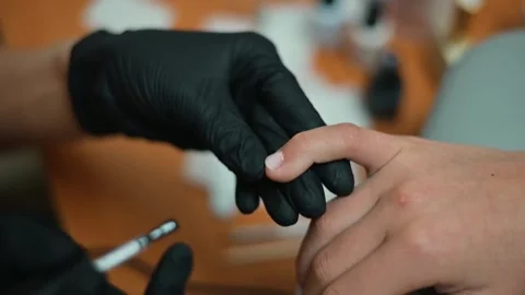 A person sits while a nail technician applies black polish to their fingernails. Stock Footage 338447534