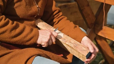 A person sits on a wooden bench, using a tool to shape a piece of wood. The Video stock 345033037