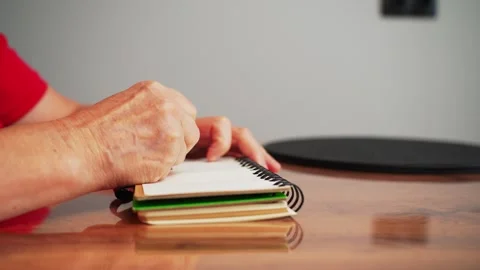 A person sits at a wooden table with a notebook in front of them. They are writi Stockbeeldmateriaal 333646577
