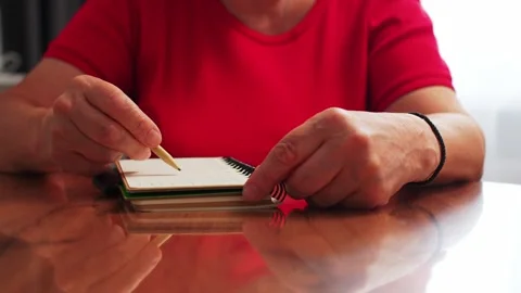 A person sits at a wooden table with a notebook in front of them. They are writi Stock Footage 334551431
