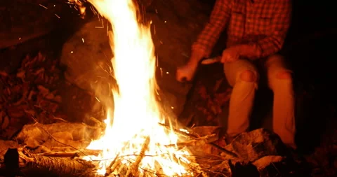 Person sitting alongside a roaring campfire outdoors at night Video stock 152851936