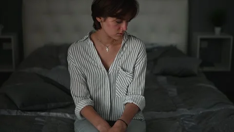 A person is sitting on a bed with a pensive expression. The indoor setting is Видео 336778510