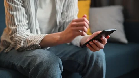 A person is sitting on a couch and using a smartphone. They frequently tap and Video stock 338446104