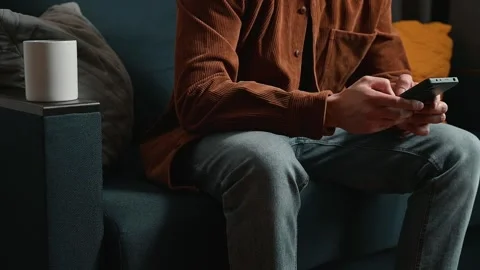 A person is sitting on a couch and using a smartphone with their hands. A white Stock Footage 339097493