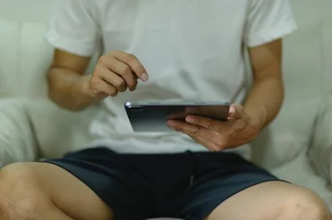 Person Sitting on Couch Using Tablet Device with Casual Clothing and Relaxe.. Stock Photos