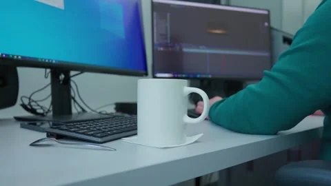 A person is sitting at a desk with 2 computer monitors and coffee cup Stock Footage 273123083