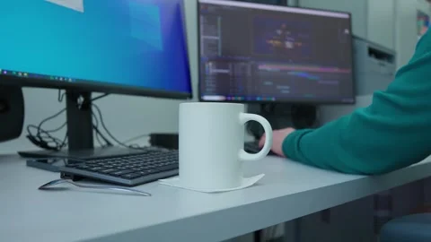 A person is sitting at a desk with two computer monitors and a white mug in the Video stock 270399027