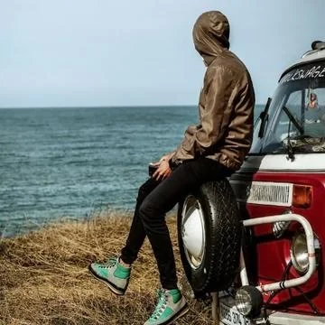 A person sitting in front of the sea on the rescue wheel of his van Stock Photos