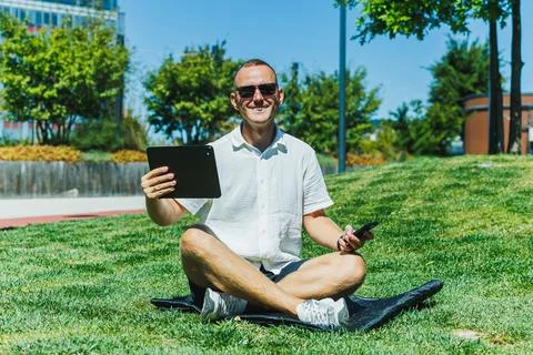 Person sitting on grass using tablet and phone during daytime in a park Stock Photos