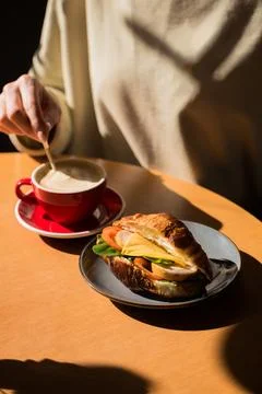 A person is sitting at a table with a cup of coffee and a croissant with fi.. Foto stock