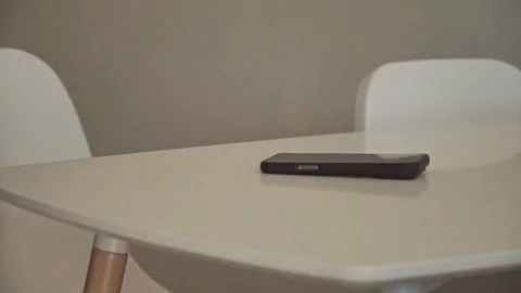 Person sitting at a table with a smartphone in front. Stockbeeldmateriaal 339826575