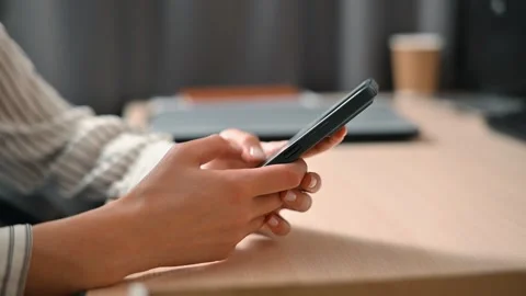 A person is sitting at a table using a smartphone with both hands. There are Stock Footage 339005916