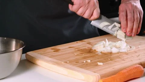 A person skillfully chops onions on a wooden cutting board in a bright kitchen 動画素材 316632179