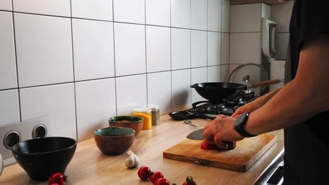 A person skillfully chops ripe tomatoes on a wooden cutting board in a Stock Footage 316478065