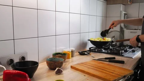 A person skillfully prepares a vegetable stir fry using a wok in a well-lit Stock-Footage 316482060