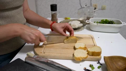 A person is slicing bread and meat with a knife on a wooden cutting board. Stock Footage 336064896