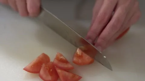 Person slicing a fresh tomato using roll-cut technique in home kitchen Stock Footage 315583272
