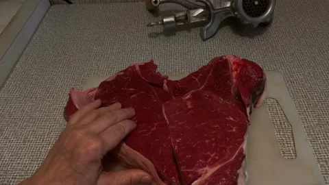 Person slicing large raw beef steaks on cutting board with meat grinder in .. Stock Footage 344422187