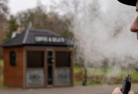A person smokes from an electronic device while standing near a small coffe.. Stockfoto's