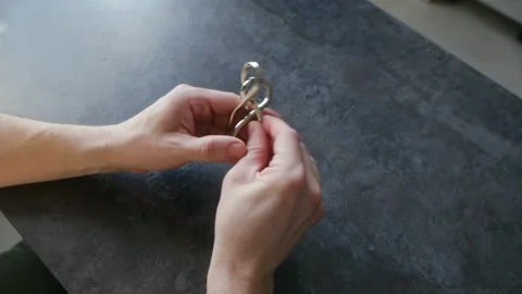 Person solving a challenging metal brain teaser puzzle Stock Footage 337892437