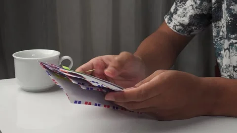 Person sorting envelopes on table with glass cup and curtain background 库存影片 276716942