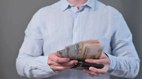 A person is sorting through cash in a wallet while standing against a plain Stock Footage 338300087