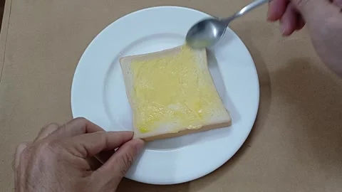 Person spreading butter on slice of bread. Top view of sandwich with butter. 스톡 동영상 260045717