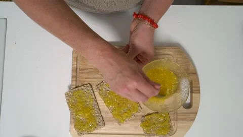 A person is spreading yellow jam onto crisp bread slices and adding round Stock Footage 336071199