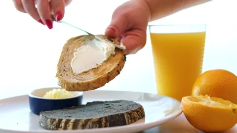 A person spreads butter onto a slice of bread at a well-lit breakfast table with Stock Footage 316094280