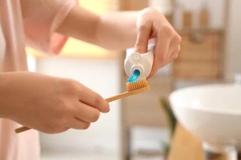 Person squeezing blue toothpaste onto eco-friendly bamboo toothbrush for dail Фото
