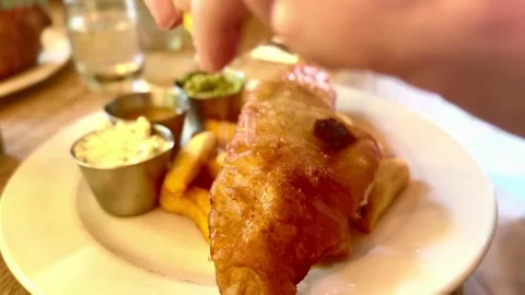 Person squeezing lemon onto battered fish and chips with condiments on plate Stock Footage 336039008
