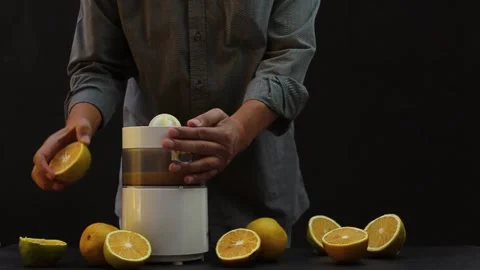 Person squeezing oranges in a machine with a black background Stock Footage 131250996