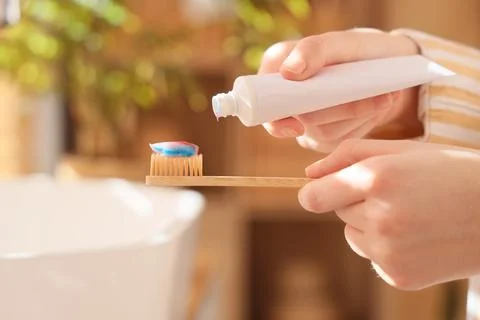 Person squeezing toothpaste onto bamboo toothbrush for oral hygiene and susta Фото