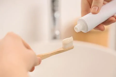 Person squeezing toothpaste onto a bamboo toothbrush in a bathroom, daily ora Фото