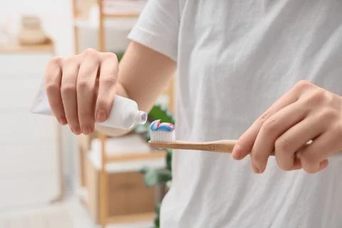 Person squeezing toothpaste onto bamboo toothbrush for oral hygiene and susta Фото