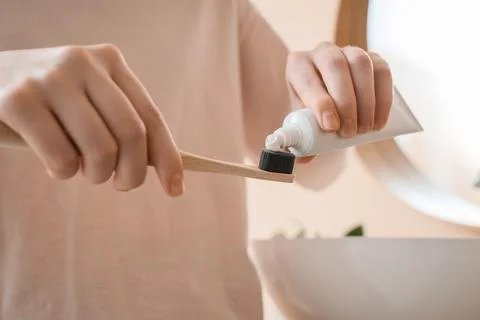 Person squeezing toothpaste onto eco-friendly bamboo toothbrush for sustainab Фото