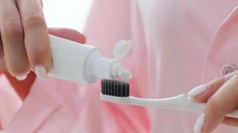 Person squeezing toothpaste onto toothbrush in pink shirt Stock Photos