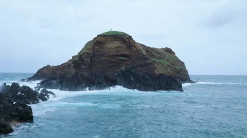 Person standing alone on a dramatic rocky islet in a stormy sea 库存影片 333695033