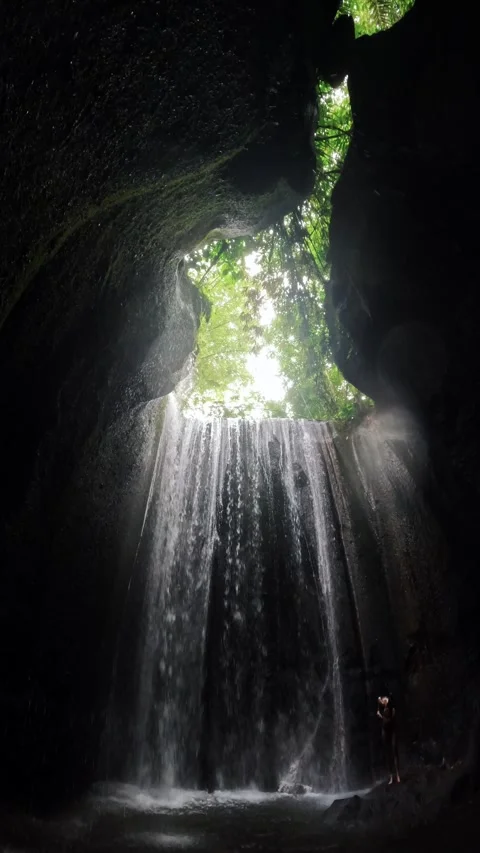 Person standing in cave under waterfall streaming through opening Stock Footage 341515923