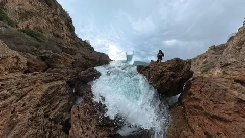 A person standing on a cliff overlooking a wave exploding into foam against the Stock Footage 293736109