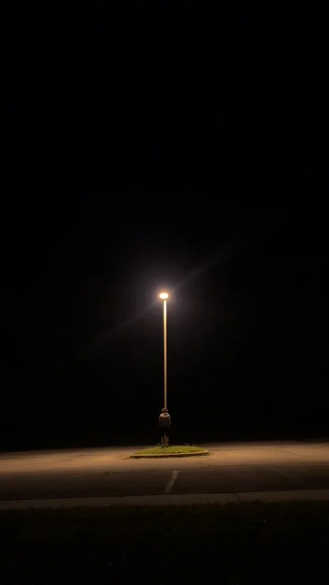 Person standing in front of lamp post up on grass in the middle of a parking lot Video stock 196221024